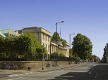 The College front range: a Georgian building in light stone, shaped like a Greek temple, with a pediment over the front entrance. A road stretching away from the camera, with trees in leaf and high street lamps.