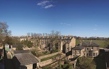 A view over the backs and gardens of a row of Georgian terrace houses in pale brown brick, with slate roofs. A wided green in the background, with clear blue sky above.