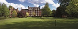 A wide expanse of lawn, with trees in leaf. In the background a red-bricked building with large white sash windows and a central doorway.