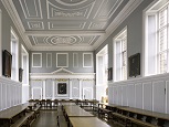 A long Georgian room with blue and white panelled walls & ceiling. High clear-paned windows on either side, with three long wooden tables and benches stretching the length of the room.