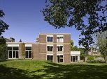 A 1960s square buildings with large windows, located in a garden with a large lawn. A clear blue sky behind.