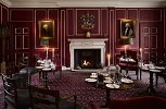 A dark red and white panelled room with paintings either side of a white fireplace. There are small tables and chairs in dark wood, laid for dessert.