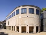 A semi-circular stone building with square archways along its base and matching windows on the top level. A clear blue sky behind.