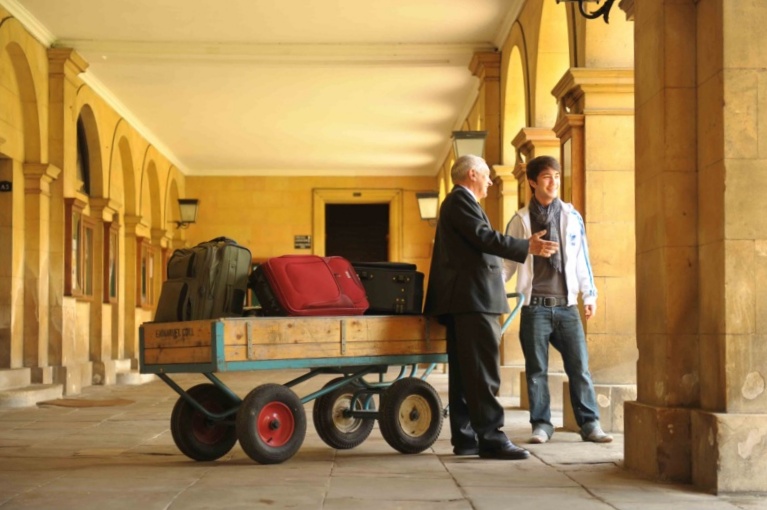 Porter & student in Porters' Cloister with trolley of suitcases