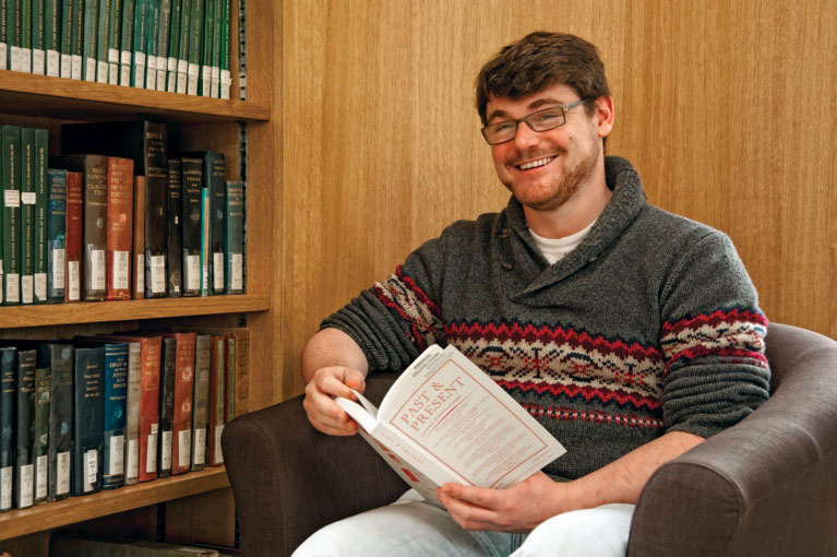 Graduate student seated in the Library, holding a book