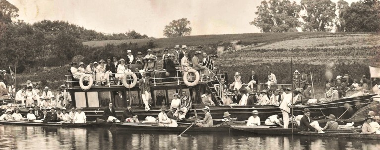 A black and white photo of a group of boats on the river with people all over them