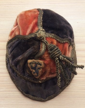 A vintage pink and blue cap with a tassel and crest on the front