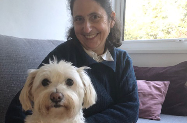 A middle aged woman on a sofa, holding a small white dog