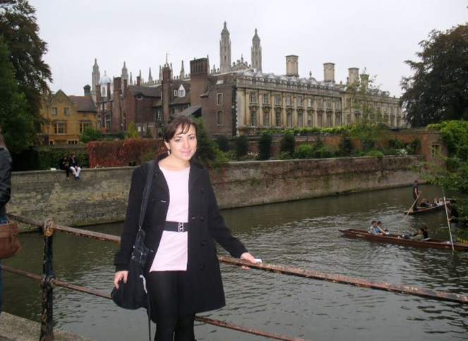 A Mexican woman standing on a bridge over a river, with a medieval building in the background