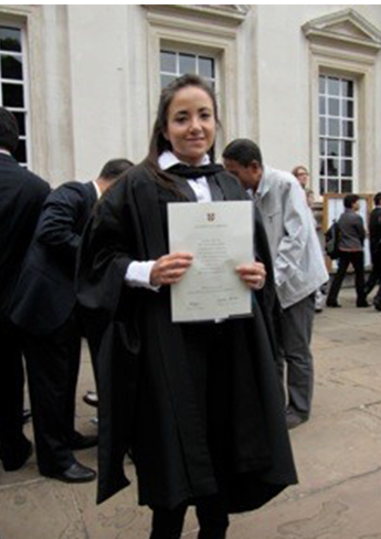 A Mexican woman in a black gown, holding a degree certificate in front of her