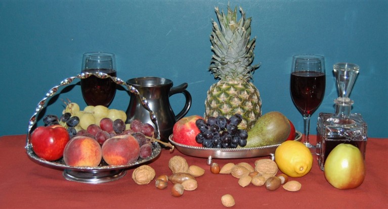 A photograph of a selection of fruit, with glasses of wine behind