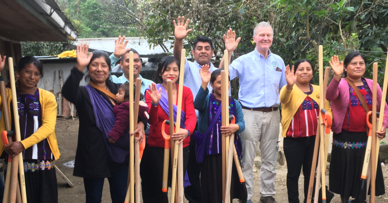 A white man standing in a group of Tzeltal Indian men & women waving at the camera.