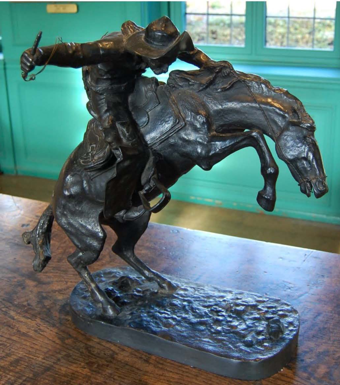 A bronze sculpture of a bucking horse, with a man on its back, wearing a hat and holding a whip.