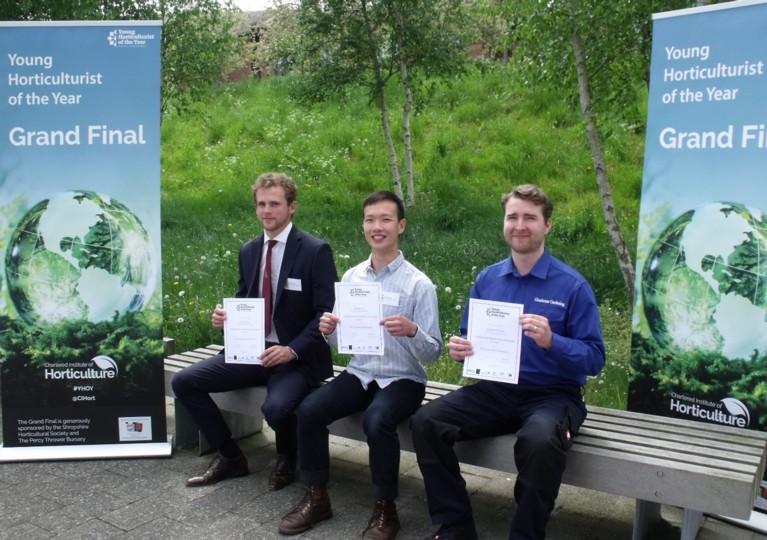 Three men sitting on a bench, holding certificates