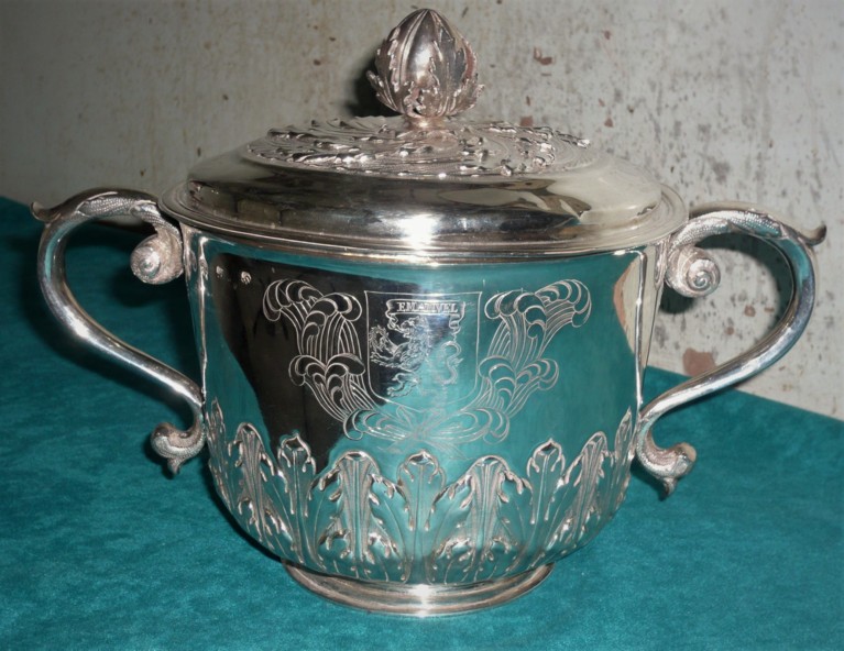 A small silver cup with two handles and a lid with a flame as a handle