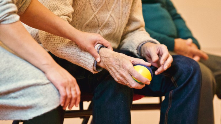 An elderly person sitting, and holding the hand of a younger person