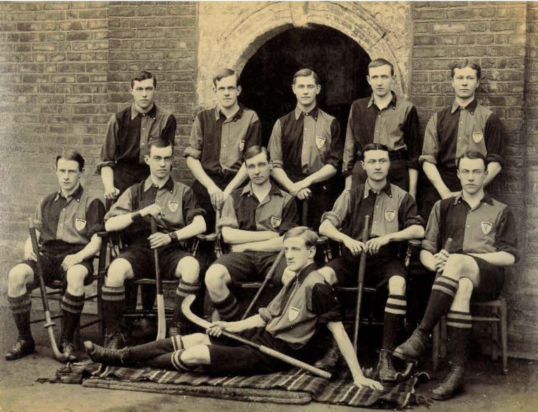 A black and white photograph of a group of students, in striped shirts, seated and standing in front of an arch