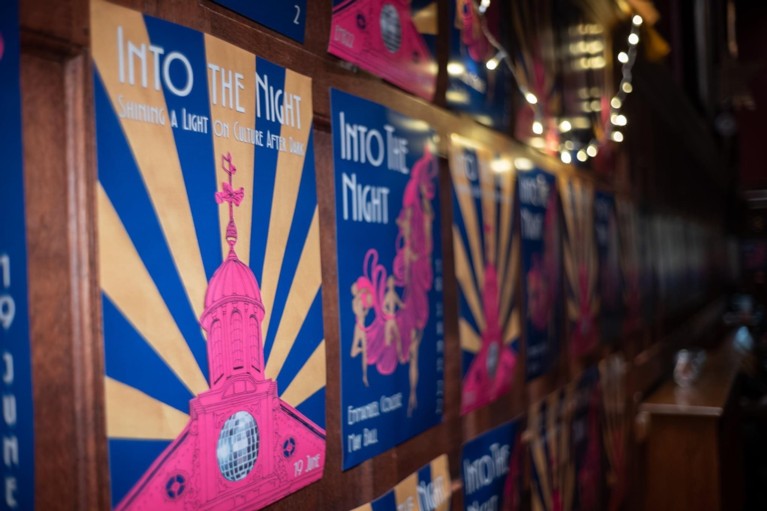A row of posters reading 'Into the Night', with a pink coloured Chapel cupola