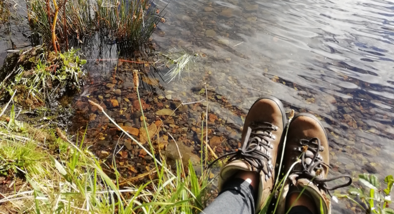 A small expanse of water, with a pair of feet in hiking boots stretched on the bank.