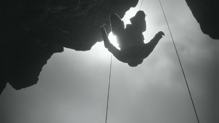 A person in silhouette, hanging on climbing ropes, from a mountain
