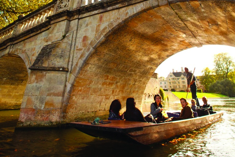 Group punting under a bridge on the Cam, with sun behind