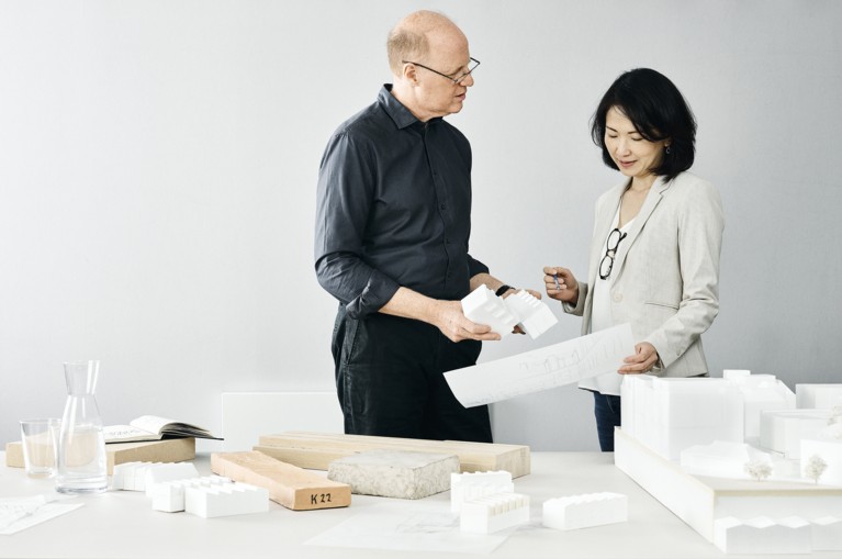 Two architects discussing designs with models and materials on a table in front